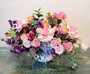 The Secret Garden is a dreamy , whimsical mixed pastel floral arrangement including pink roses, purple, blue hydrangeo with purple accent pom style mum blooms, tulips and seasonal garden flowers arranged in a white modern bowl vase hand crafted by Lexis Florist Houston