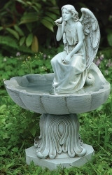 Angel sitting in birdbath statue sitting in grass outdoors.