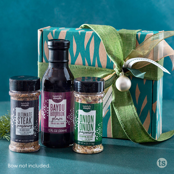 Tastefully Simple Ultimate Steak™ Seasoning, Bayou Bourbon™ Glaze, and Onion Onion™ Seasoning displayed in front of a wrapped gift box.