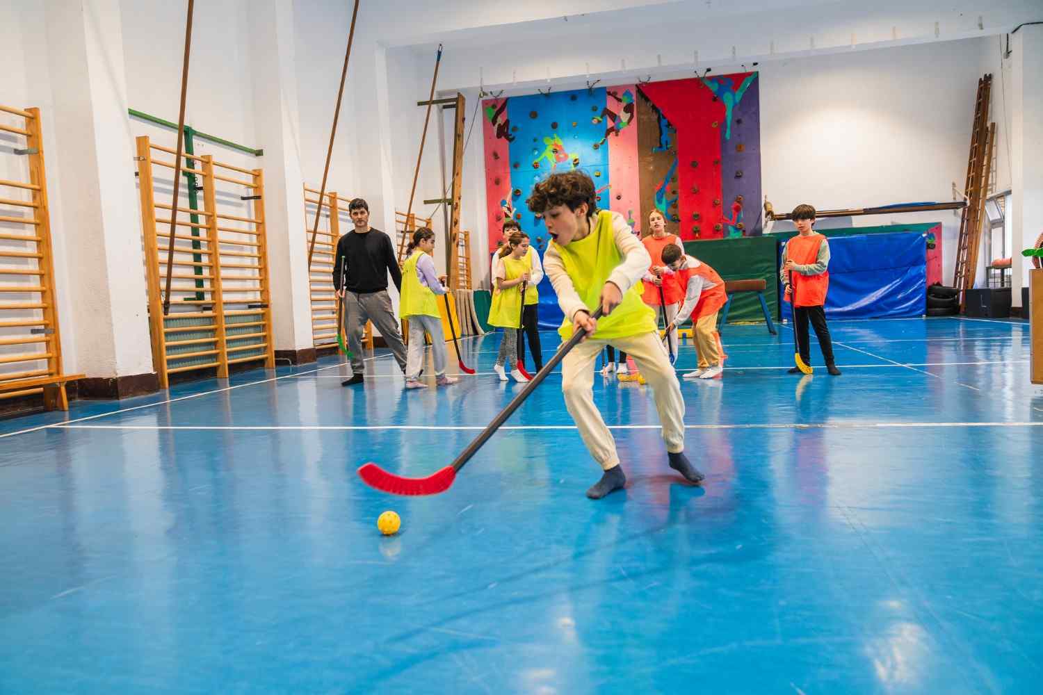 Photograph of children playing floor hockey in a gymnasium with blue flooring
