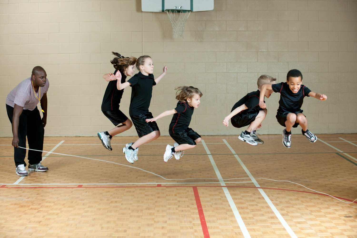 Photograph of five children in black athletic clothing jumping over a long rope