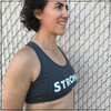 Looking for the perfect sports bra to wear to the gym on lifting or cardio days? This is a side view of the Strong Sports Bra by Strong Athletic. The word Strong is printed in bold, distressed white letters across the chest. The design of the bra has two seems running on the outside of the bust, making it so the shape of the chest when wearing the bra is very complimentary. 