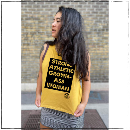 This is the Strong Athletic Grown-Ass Woman Crop Top in mustard fabric with black ink. We created this tank to give women something fluid and soft to wear while working out or going to work. This tank is cut at the arms to make it look like you cut the sleeves off of your favorite t-shirt. 