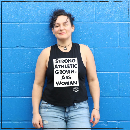 This is the front of the Strong Athletic Grown-Ass Woman Crop Top Racerback Tank Top in Black with White Ink by Strong Athletic. Know any grown-ass women? We do! We print this design on the Bella Canvas 6682 Crop Top Racerback Tank. All Bella shirts are made at a W.A.R.P. Certified facility.  Strong Athletic is a woman-owned company, our goal is to highlight the fact that many women, girls and LGBTQIA2S+ athletes are not given the same opportunities as their male counterparts in sports. We want to help to change this. 
