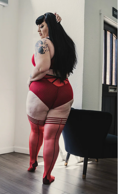 Plus size female model wearing  red lingerie and showing Kix'ies, red retro thigh high stockings with Cuban heels, black back seam and 3 band silicone tops. Plus size female model wearing  red lingerie and showing Kix'ies, red retro thigh high stockings with Cuban heels, black back seam and 3 band silicone tops.