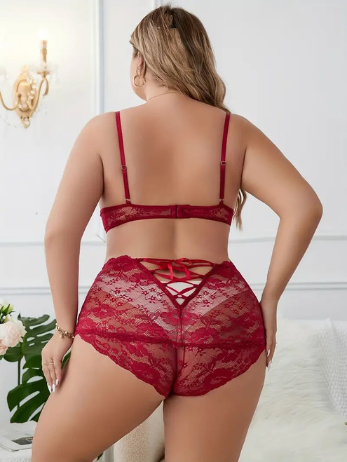 Female lingerie model wearing a red, floral lace bra with red over bust straps and matching red floral lace booty shorts with satin ribbon lace up rear.
