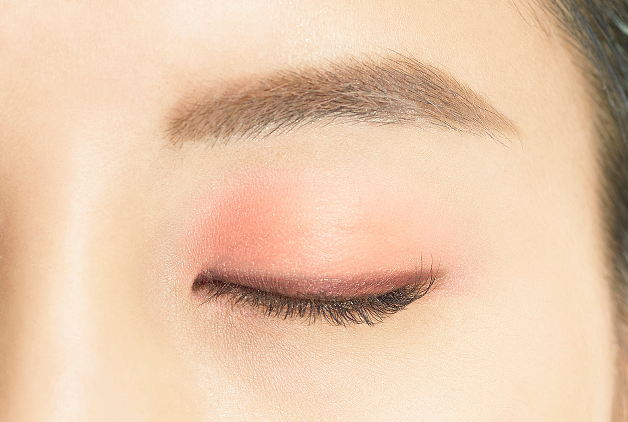 Image showing Dual Colour Stick in PK02 Époque Pink applied to the eye. There is a line of dark reddish  brown close to the lash line, with a light wash of warm peachy pink over the rest of the lid creating a gradient effect.