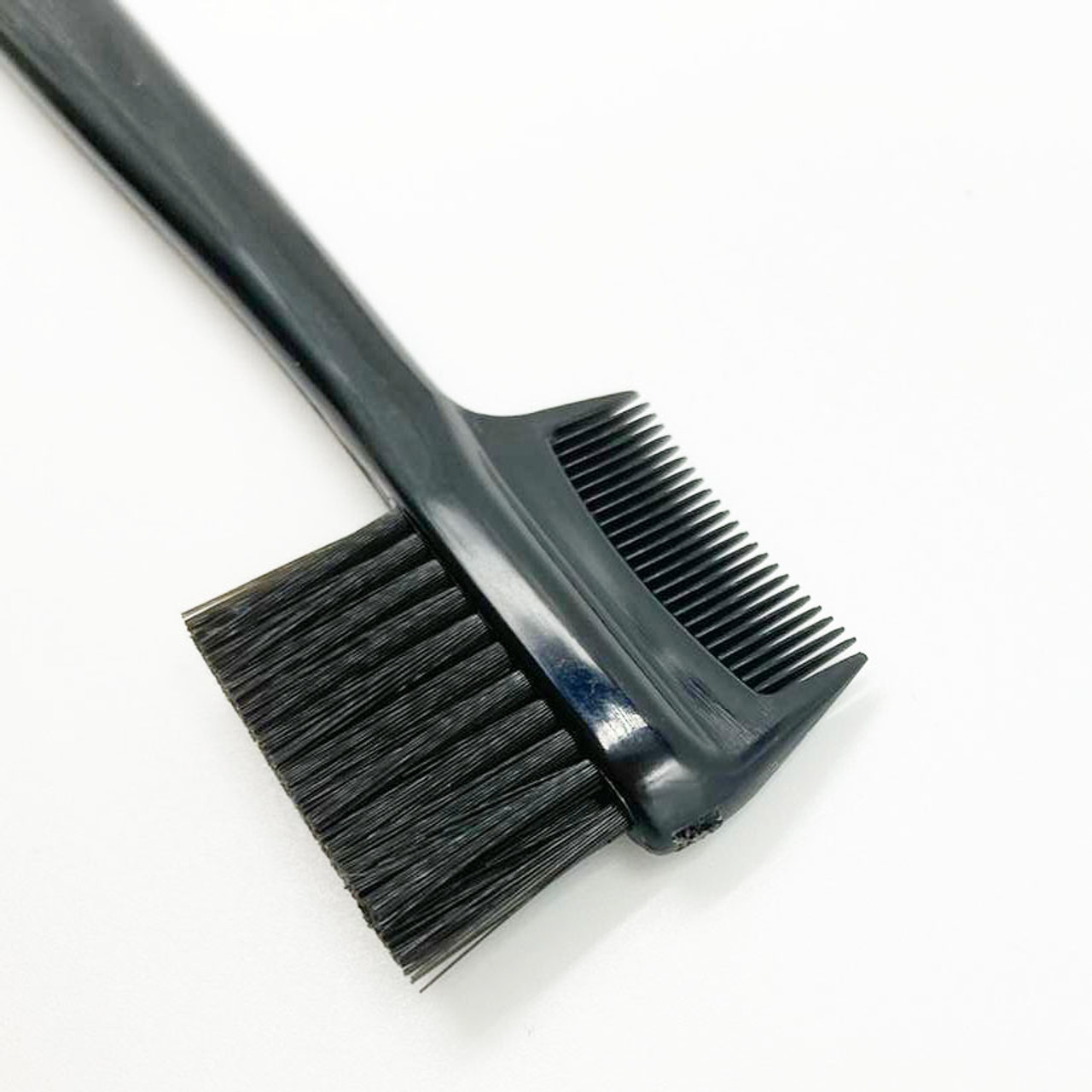 The Brow Brush & Comb is pictured, it a comb on one side and on the back of the comb is a nylon brush with dense bristles. It has a long black handle with the Mary Quant Daisy printed on it.