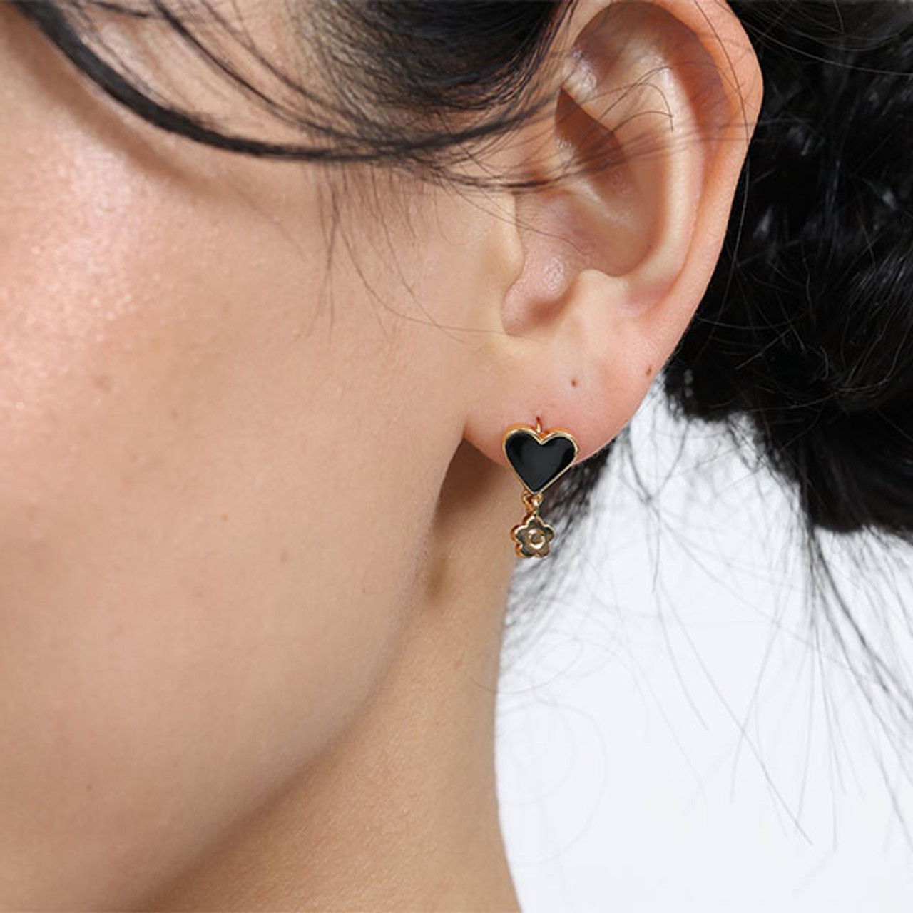 Black heart shaped resin earrings with a small gold Mary Quant daisy dangling from the bottom of the heart as worn by a model.