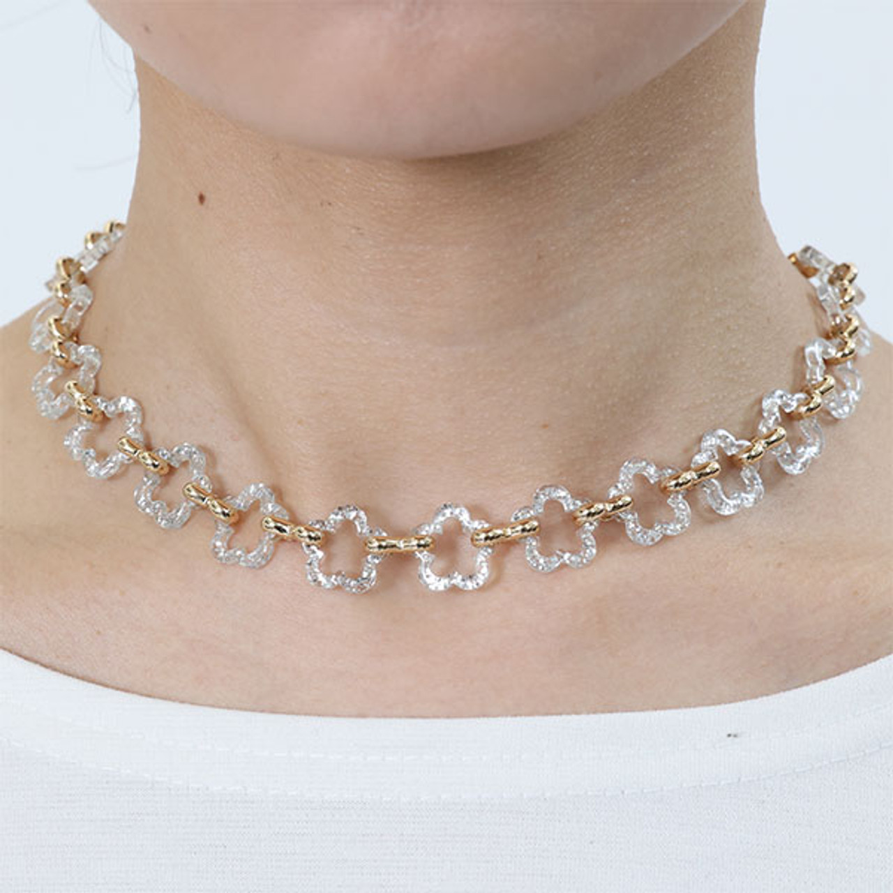 A model wearing the Acrylic Daisy Chain necklace in clear. The necklace is short and has a gold chain. Clear daisy outlines loop together to form a chain.