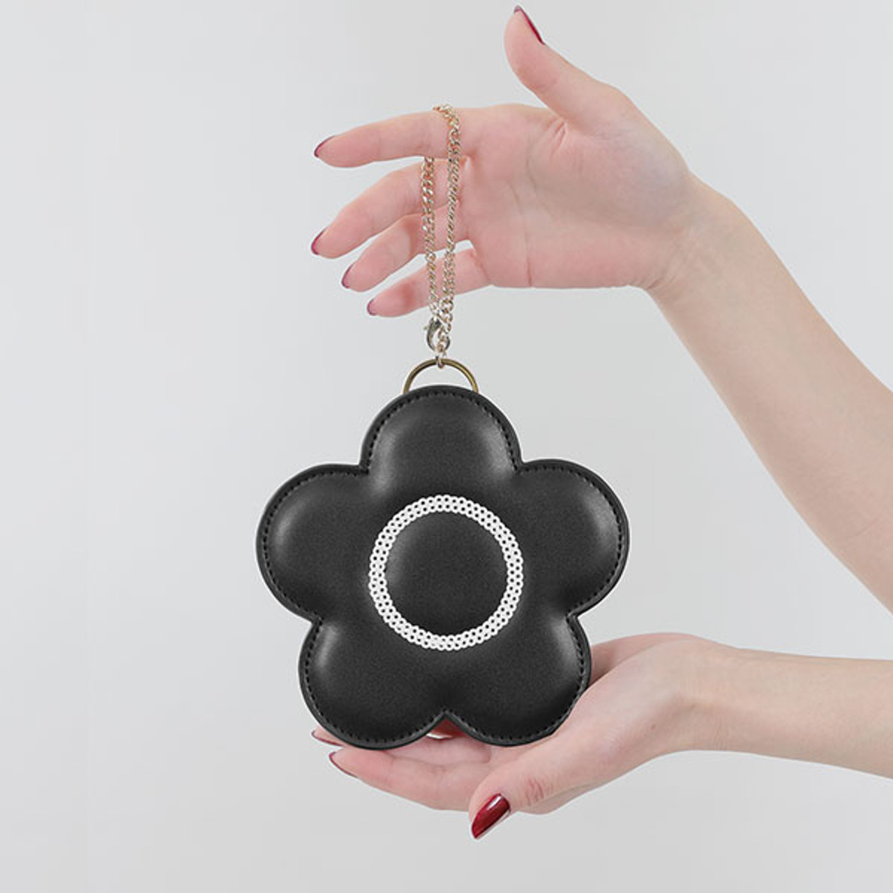 A model holds the black daisy shaped mini pouch. There is a circle of silver sequins around the centre of the daisy and there is a gold chain to attach the pouch to your bag.