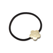 The daisy hair tie in gold. A sleek metal daisy is threaded onto a simple black band.