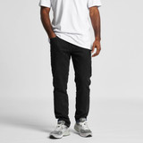 A pair of black jeans worn by a person, paired with a white t-shirt and grey sneakers. The jeans feature a branding logo.