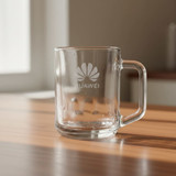 A glass mug with a handle, featuring a logo, placed on a wooden surface.