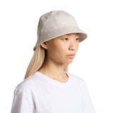 A bucket hat in a light beige colour, featuring a logo, displayed on a model with long hair.