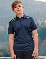 A boy stands outdoors wearing a navy polo shirt with yellow accents and a logo. The background features trees and hills.