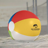 A beach ball with red, yellow, blue, and green panels, featuring a logo, resting on sandy ground.