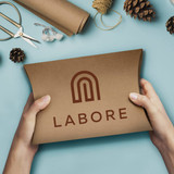 A person holding a brown, extra-large pillow box with a logo, surrounded by crafting materials and pinecones.