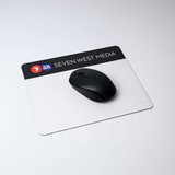 A black mouse sits on a rectangular, white mouse mat with a logo at the top. The mat has a natural rubber base.