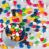 A tin filled with assorted mini jelly beans in vibrant colours, surrounded by more scattered jelly beans.