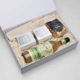 A white gift box containing a drink bottle, two small boxes, and a bag of pretzels, all in neutral tones.