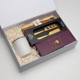 A gift box containing a cheese board, gold cheese knives, and a ceramic container, all set in white paper fill.