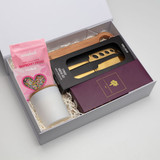 A gift box containing a knife set, a wooden utensil, a candle, and pink chocolate-covered frogs.