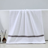 A white bath towel with a grey stripe hanging over a bathtub, accompanied by decorative items beside it.