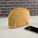 A yellow kraft paper cosmetic bag with a rounded shape and a zip closure, placed next to a smartphone.