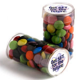 A clear tube containing colourful choc beans in various hues, with a branding sticker on the lid.