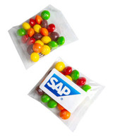 A sealed bag containing a mix of colourful Skittles in yellow, green, red, orange, and brown, with a branded sticker.