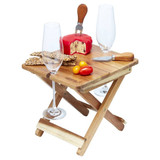 A foldable wooden cheese and wine board with a cheese block, knife, crackers, and two glasses.