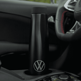 A drink bottle in matte black with a logo, placed in a car cup holder.
