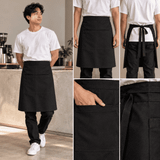 A black half bib long apron with a pocket, featuring a tie at the back and worn by a model in a café setting.