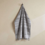 A flat terry towel in shades of grey, hanging neatly with fringed edges. It features a logo on the fabric.