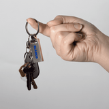 A hand holds a silver keychain attached to several keys, featuring a logo. The overall look is sleek and modern.