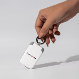 A white mini power bank with a keyring attachment is held by a hand, featuring a logo on its side.