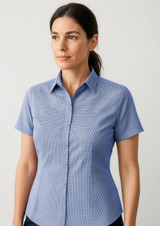 A short-sleeve button-up shirt in light blue, featuring a checkered pattern and a collar. It has a logo on it.