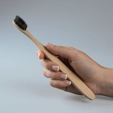 A bamboo toothbrush held in a hand, featuring a natural wooden handle and black bristles.