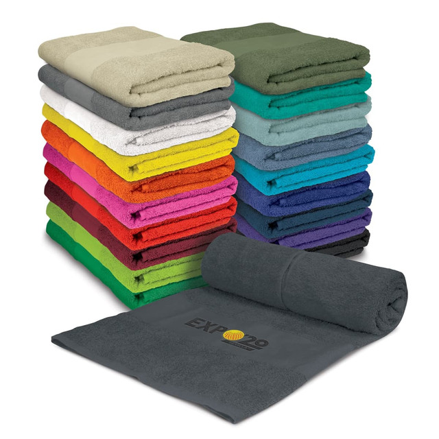 A stack of colourful beach towels in various shades, with one grey towel partially rolled out and displaying a logo.