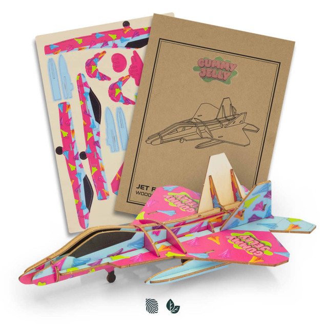 A vibrant pink and blue wooden jet fighter model with assembly instructions in the background.