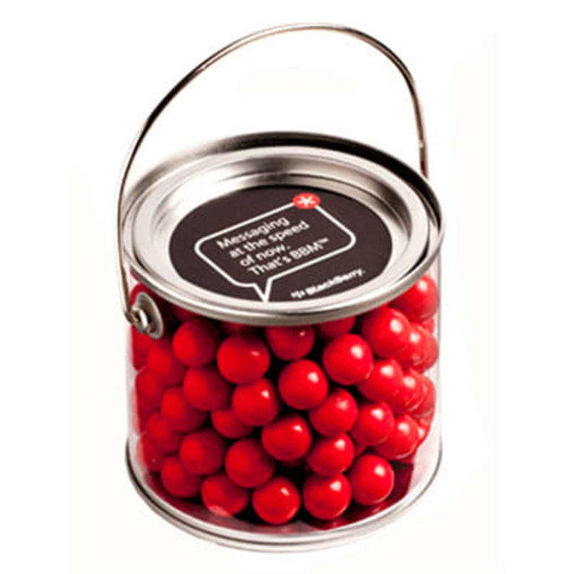 A medium PVC bucket filled with vibrant orange chocolate drops, featuring a handle and a logo on the lid.