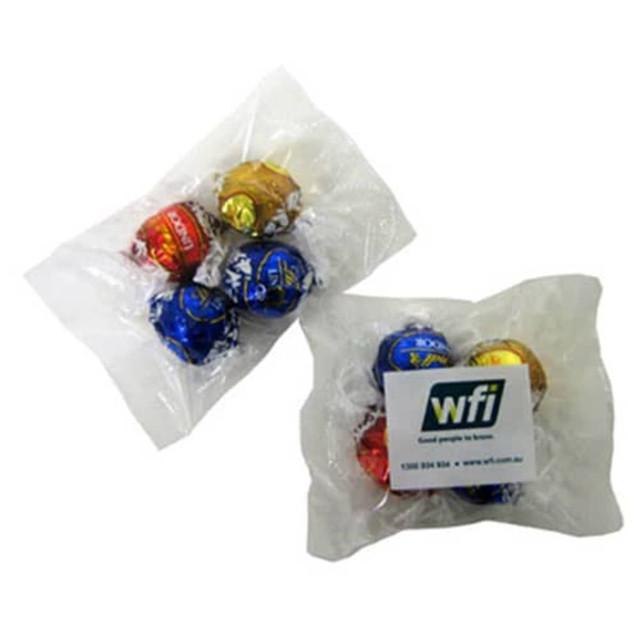 Four wrapped chocolate truffles in red, gold, blue, and silver packaging, presented in two plastic bags.