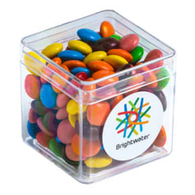 A clear cube filled with colourful chocolate beans, featuring a logo on the side.