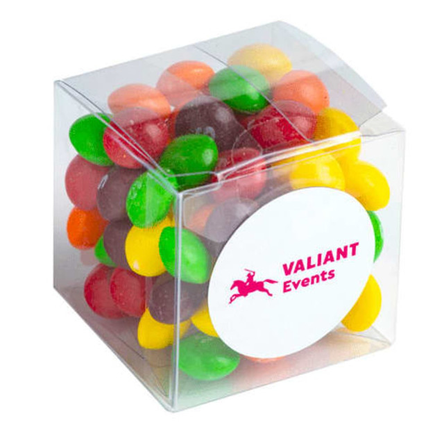 A clear cube filled with colourful Skittles in various shades of red, green, yellow, orange, and purple.