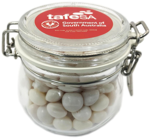 A glass canister filled with white chewy mints, featuring a lid and a logo on the top.
