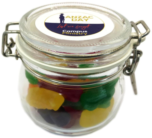 A glass canister filled with colourful jelly babies in green, yellow, red, and purple, featuring a logo on the lid.