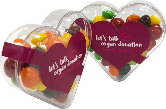 Acrylic heart-shaped container filled with colourful Skittles, featuring a logo on one side.