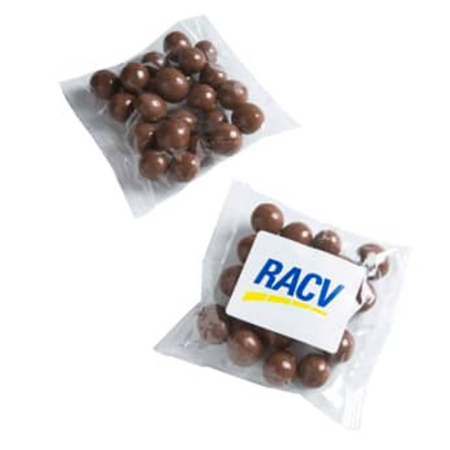 Chocolate-coated coffee beans in a clear packet, featuring a white label with a logo. Brown and glossy in appearance.