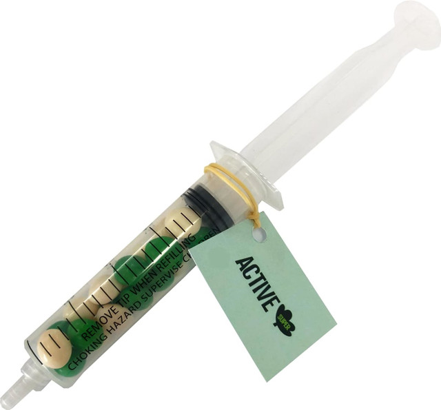 A syringe filled with chewy fruit in green and yellow, featuring a tag and a logo.